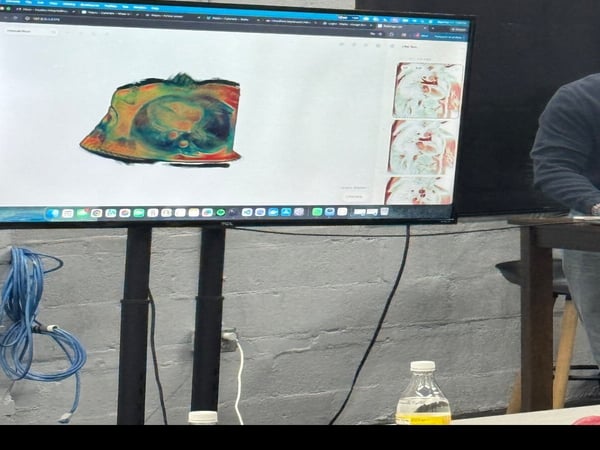 A computer monitor displaying a colorful abstract image is mounted on a stand against a white brick wall.