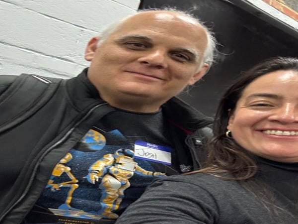 A selfie of a man and a woman smiling, with the man wearing a nametag that reads 'Josh'.