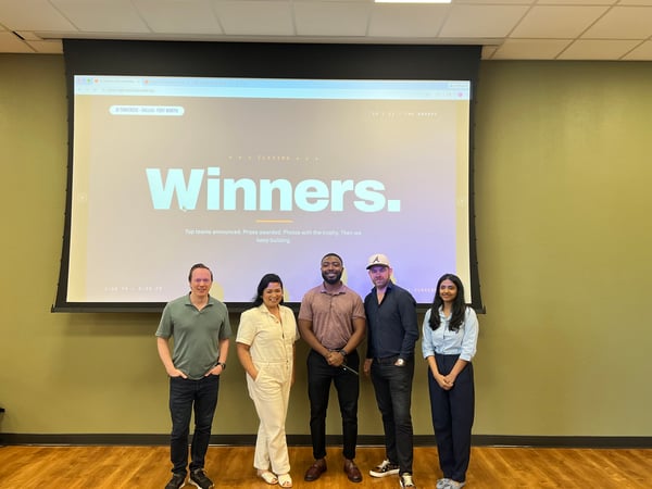A group of five people posing for a photo in front of a large projection screen that displays the word 'Winners.'