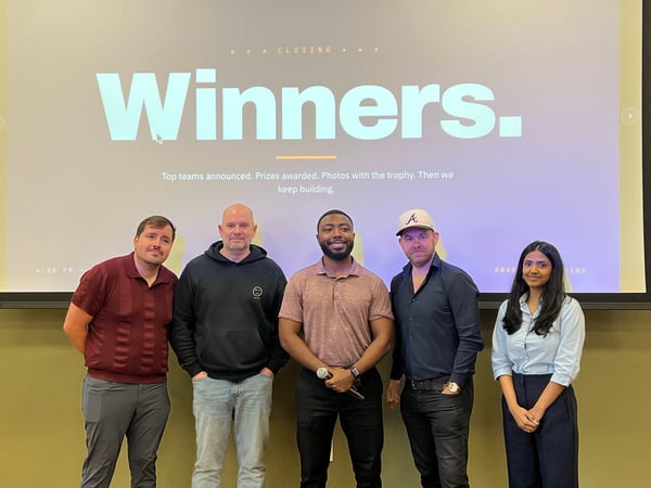 A group of five people posing for a photo in front of a large presentation screen that reads 'Winners.'
