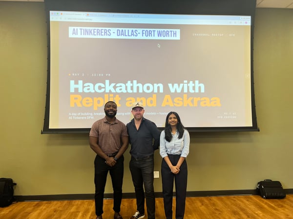 Three individuals are posing for a photo in front of a large projection screen announcing an AI Tinkerers hackathon event in Dallas-Fort Worth.