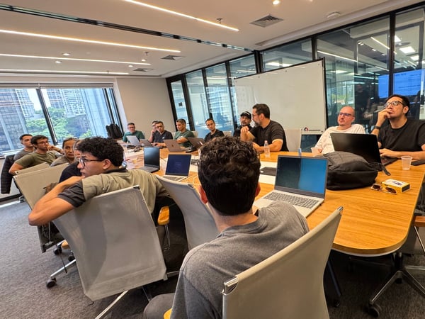 A group of people are gathered around a large wooden table in a modern office conference room, likely for a meeting or collaborative session.