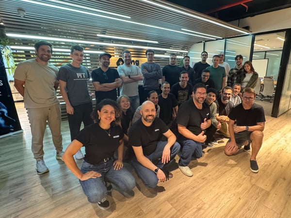 A large group of people posing for a group photo in a modern office or event space with wooden floors and glass walls.