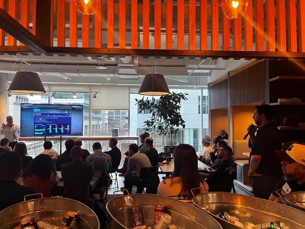 A group of people attending a tech presentation or demo in a modern indoor space with a large screen displaying data and drinks in the foreground.