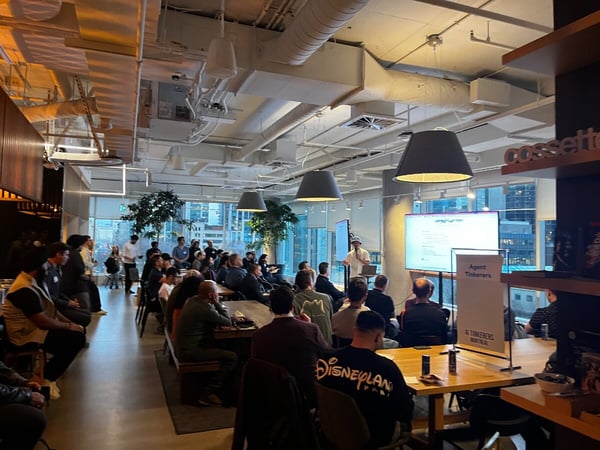 A group of people are gathered in a modern, industrial-style office space for a presentation titled 'Agent Tinkerers' by AI Tinkerers Montreal.