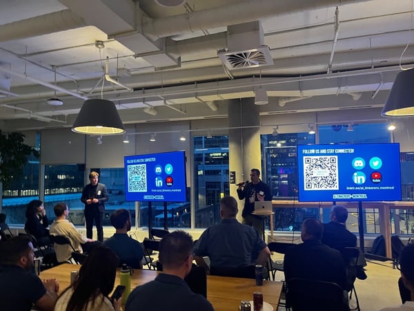 A person is giving a presentation in an office setting at night, with two large screens displaying social media information to an audience.