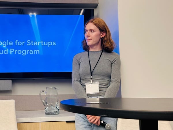 A candid photograph of a person, likely a presenter, standing in a modern conference room in front of a large screen displaying the text 'Google for Startups Cloud Program.'