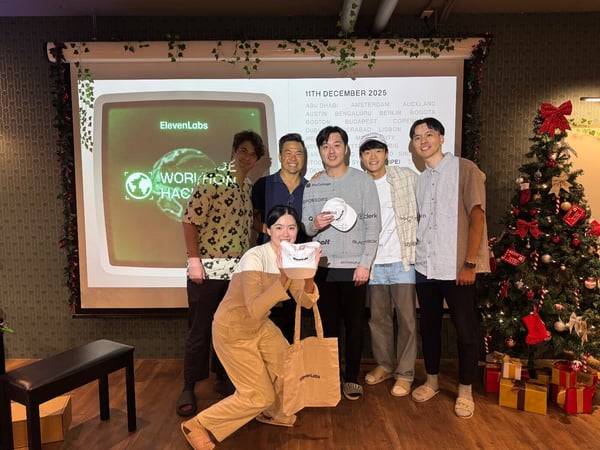 A group of six young adults, likely participants or organizers of a hackathon or workshop, pose indoors in front of a projection screen displaying event details and next to a decorated Christmas tree.