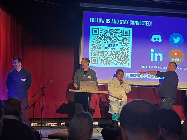 A group of presenters on a stage during an 'AI Tinkerers Montreal' event, with a projector screen showing a QR code and social media links.