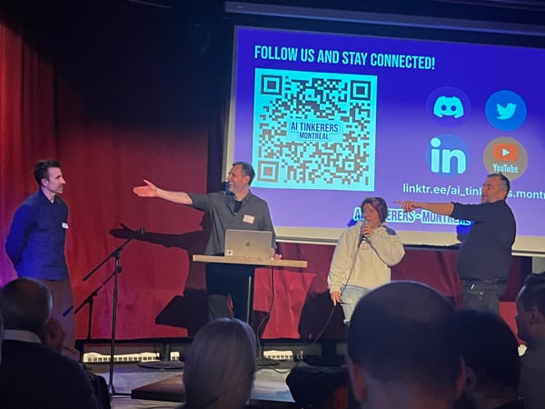 A group of people are on a stage during an AI Tinkerer's Montreal event, with one person speaking into a microphone in front of a presentation screen.