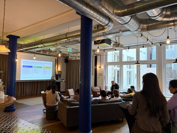 A man is giving a presentation about 'Cloud Run' to a small audience in a modern, industrial-style office space with blue pillars and exposed ceiling pipes.