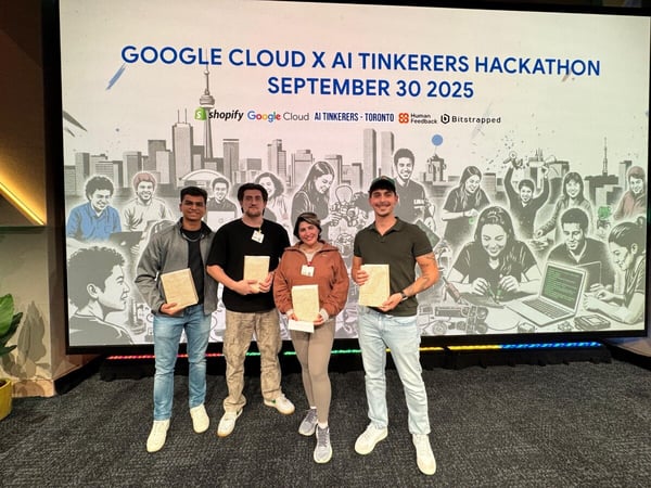 A group of four people, likely winners or participants, pose for a photo in front of a large screen displaying the branding for the 'Google Cloud X AI Tinkerers Hackathon.' They are holding small awards or plaques.