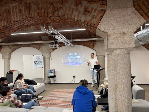 A man is giving a presentation titled 'Red Bull Basement' to a small audience in a room with distinctive arched brick ceilings and stone pillars.