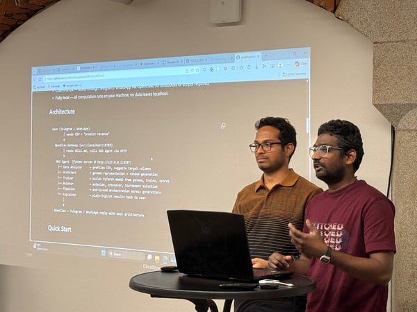 Two men are giving a technical presentation in front of a projection screen that displays a software architecture diagram.