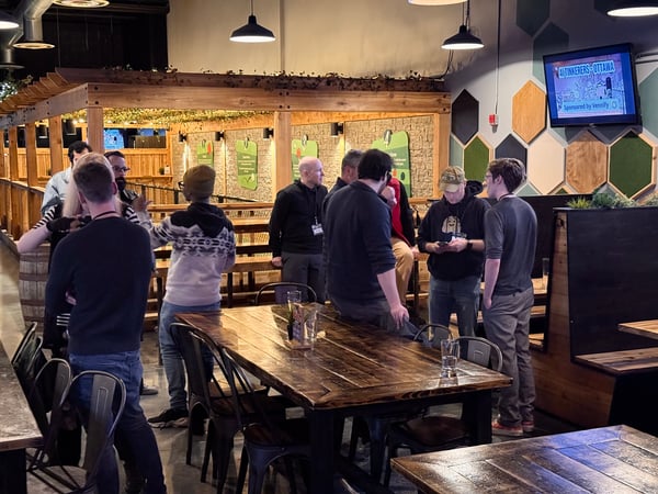 A group of people are gathered in an indoor social space, likely a brewery or restaurant, for a tech-related meetup event.