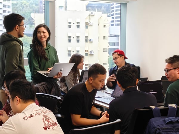 A group of young professionals are gathered in a bright office space, engaged in a collaborative discussion with laptops open on a table.