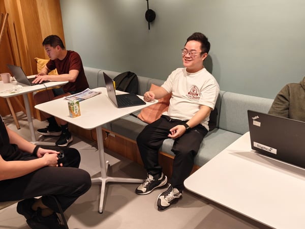 Four men are gathered in a modern coworking space, some working on laptops while others are engaged in a conversation.