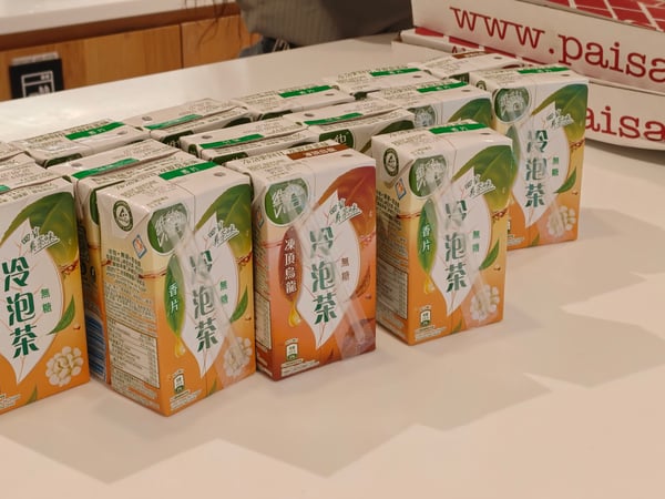 A collection of Vita brand tea cartons and Paisanos pizza boxes are arranged on a white countertop.