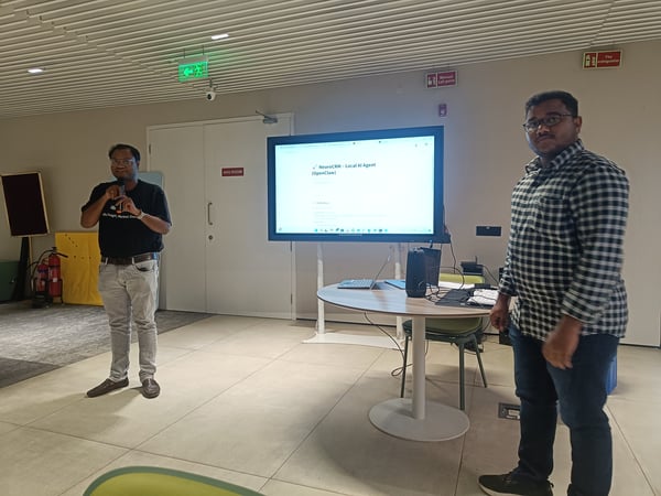 Two men are in a modern indoor space during a presentation; one man holds a microphone while a large screen displays 'NeuroCRM - Local AI Agent (OpenClaw)'.