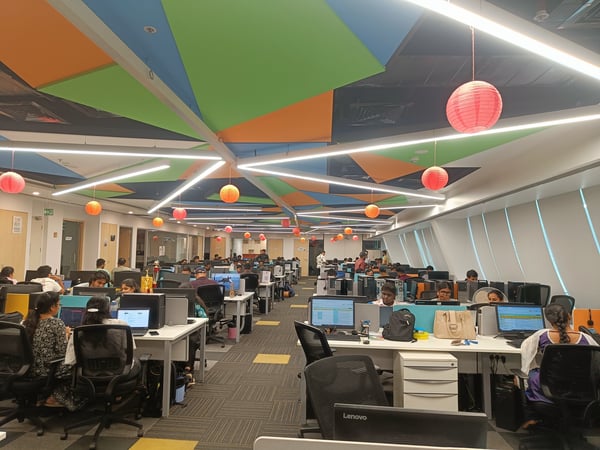 A wide-angle photograph of a large, modern office space filled with employees working at rows of desks under a distinctive, colorful geometric ceiling.