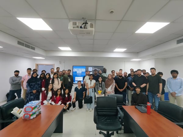 A group photograph of attendees posing together in a conference room in front of a screen displaying 'AI Tinkerers Dubai'.