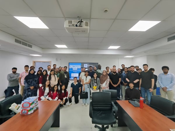 A large group of people posing for a group photo inside a classroom or meeting room with a presentation screen in the background.