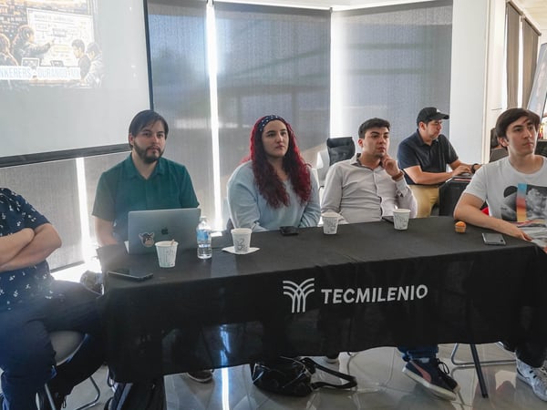 A group of people sitting at a table during an event, with a projection screen in the background displaying 'AI TINKERERS - DURANGO MX'.