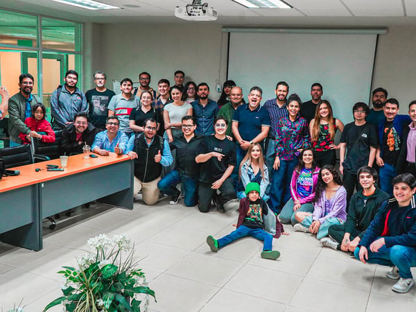 A large group of approximately 30 people is posing for a group photograph inside a classroom or meeting room.