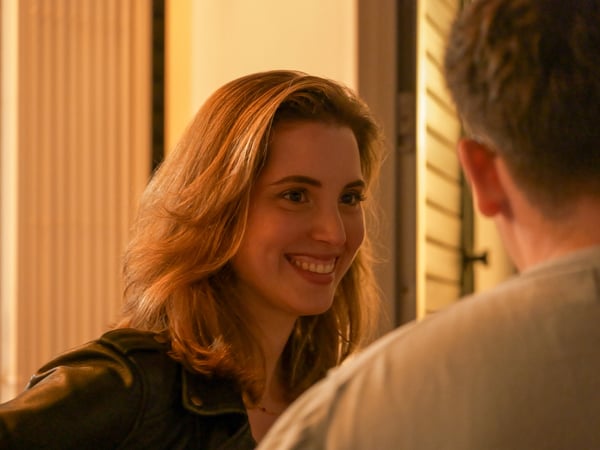 A young woman with reddish-brown hair smiles warmly while looking at a man whose back is turned to the camera.