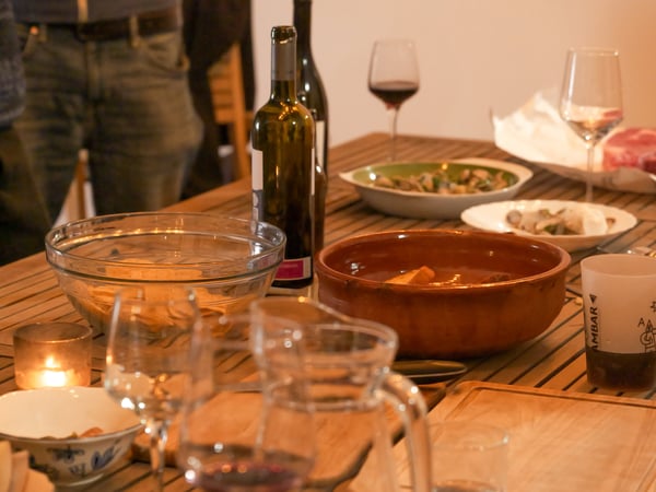 A wooden dining table is set with various dishes, wine bottles, and glasses, suggesting a social gathering or dinner party.