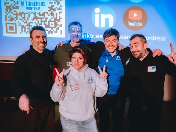 A group of five people are posing for a photo in front of a projection screen displaying event information for 'AI Tinkerers Montreal'.