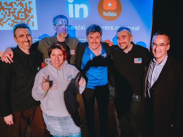 A group of six people, five men and one woman, are posing for a photograph in front of a projection screen at an indoor event.