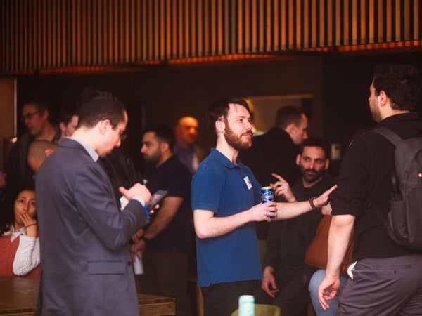 A group of people are socialising at an indoor event, with some individuals engaged in conversation while holding drinks.