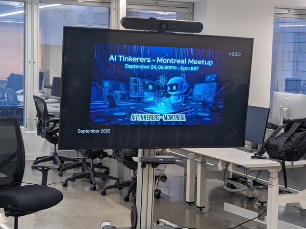 A photograph taken inside a modern, empty office or meeting room, focusing on a large screen displaying promotional material for an "AI Tinkerers - Montreal Meetup" scheduled for September 2025.