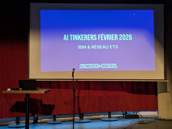 A photograph of a presentation stage featuring a projector screen displaying text for an 'AI Tinkerers' event in Montreal.