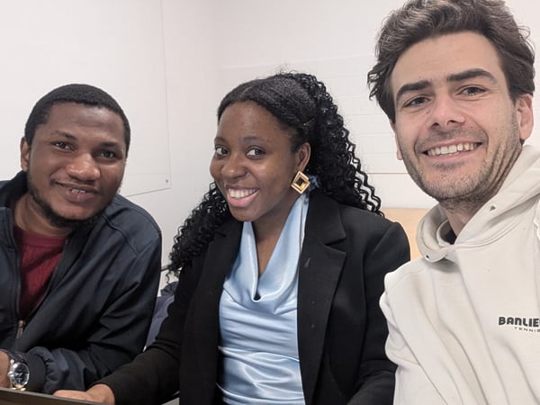 A group of three smiling people, two men and one woman, posing for a selfie-style photo in an indoor setting.