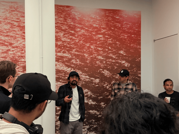 A candid indoor photo showing a group of people gathered in a modern meeting space featuring large abstract red wall art and a whiteboard, suggesting a presentation or discussion is taking place.