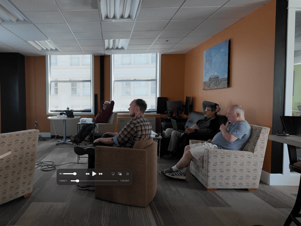 A group of men are gathered in an office space with orange walls, watching a presentation titled 'Controlled Generative UI' on a projector screen.