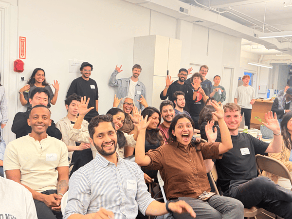 A large, diverse group of people posing for a photo in a bright, modern office space, with many individuals smiling and waving at the camera.