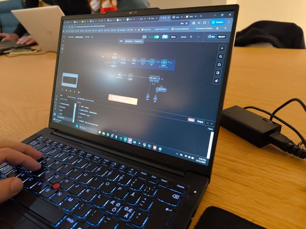 A close-up photograph shows a person typing on a black laptop with a blue backlit keyboard, displaying a dark-themed application featuring a node-based workflow diagram.