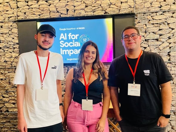 Three people posing for a photo in front of a screen displaying 'AI for Social Impact' at a Google DeepMind event.