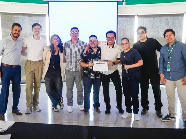 A group of nine people are posing for a commemorative photo in a modern room, with two individuals in the center holding up a certificate of recognition.