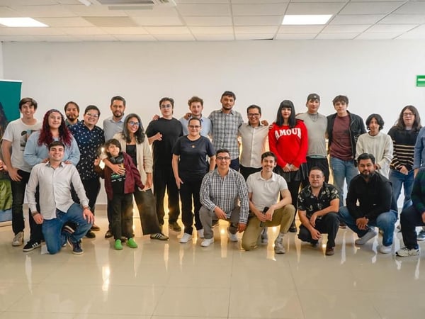 A group of approximately 24 people posing for a group photograph in a brightly lit indoor office or event space.