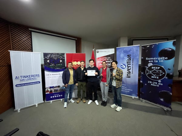 A group of five people stands in a line in front of several informational banners at an indoor event, with one person holding a certificate.