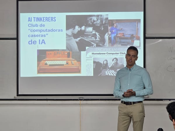 A man is standing in front of a projection screen giving a presentation about the history of personal computing and AI tinkerers.
